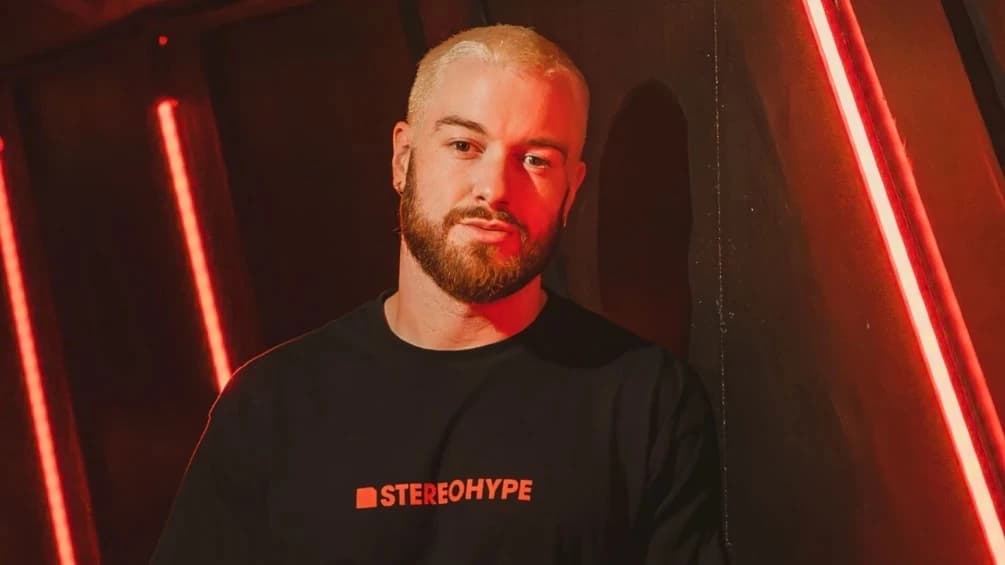 James Hype w czarnej koszulce STEREOHYPE na tle czerwonych neonów