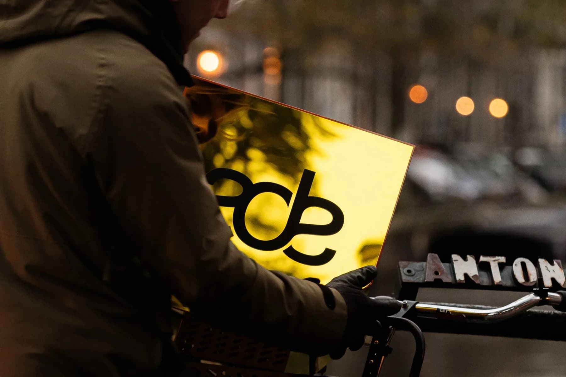 Rowerzysta wiozący ulicą Amsterdamu złotą tablicę z logotypem ADE, zdjęcie o zmierzchu