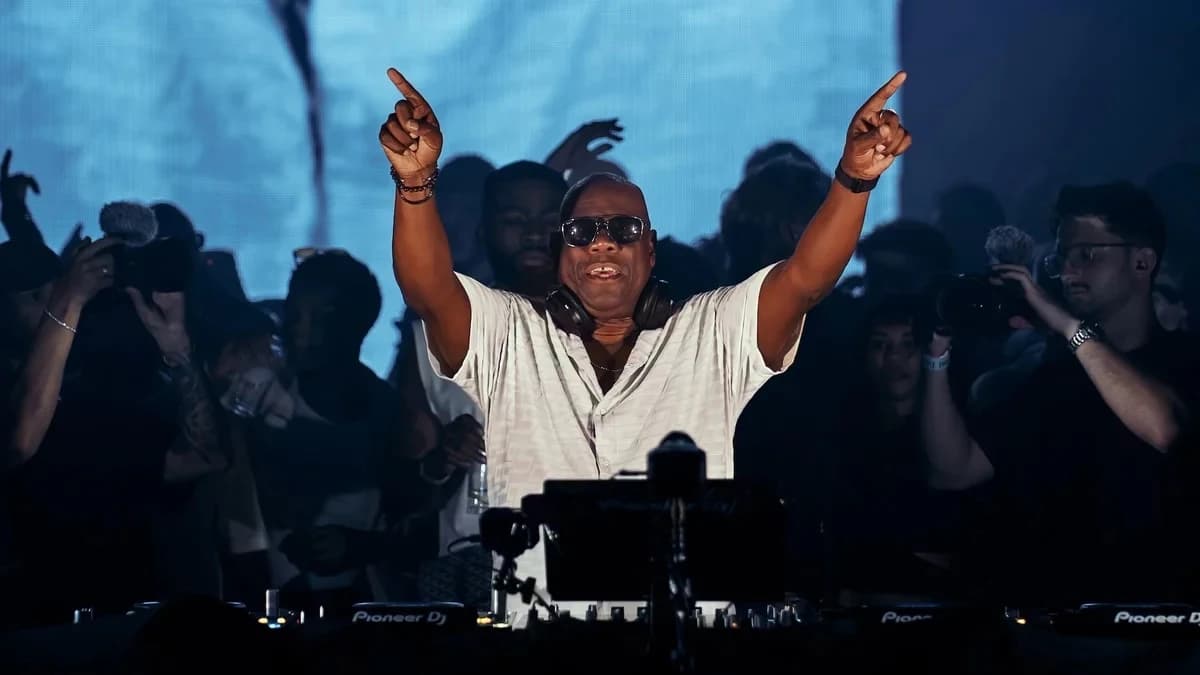 Carl Cox za konsolą Pioneer DJ z uniesionymi rękami, w ciemnych okularach i słuchawkach na szyi, przed nim publiczność z telefonami
