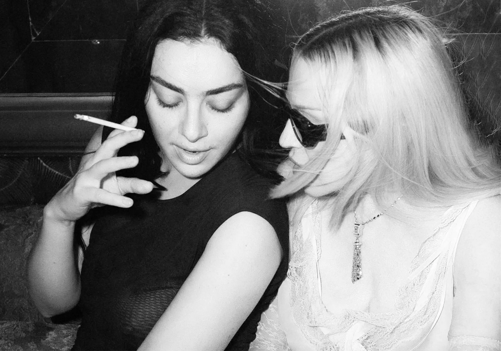 Czarno-białe zdjęcie prasowe: Charli xcx z papierosem w dłoni i Madonna w ciemnych okularach siedzą obok siebie